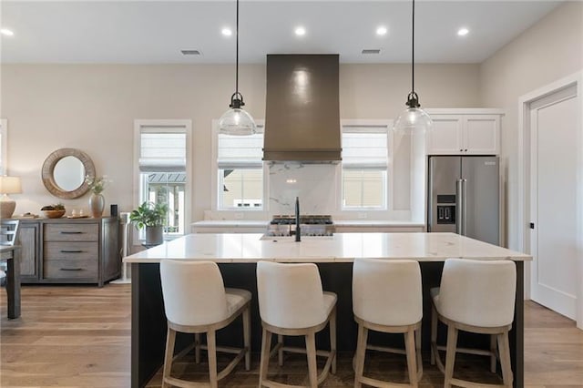 kitchen featuring a large island, stainless steel appliances, premium range hood, pendant lighting, and white cabinets