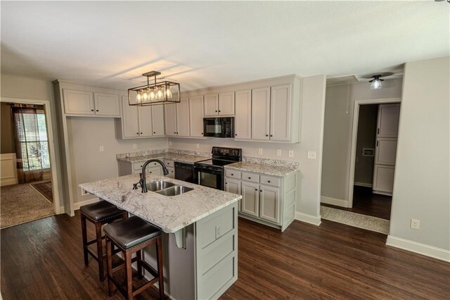 kitchen featuring light stone counters, a sink, baseboards, dark wood-style floors, and black appliances