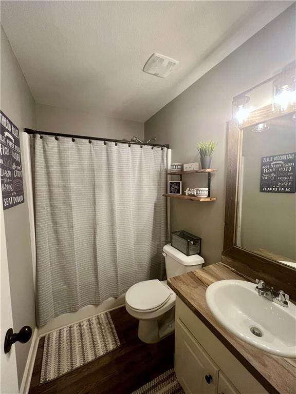 full bathroom featuring visible vents, shower / tub combo with curtain, vanity, wood finished floors, and toilet