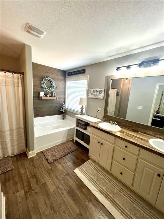 full bathroom with a garden tub, a textured ceiling, visible vents, wood finished floors, and a sink