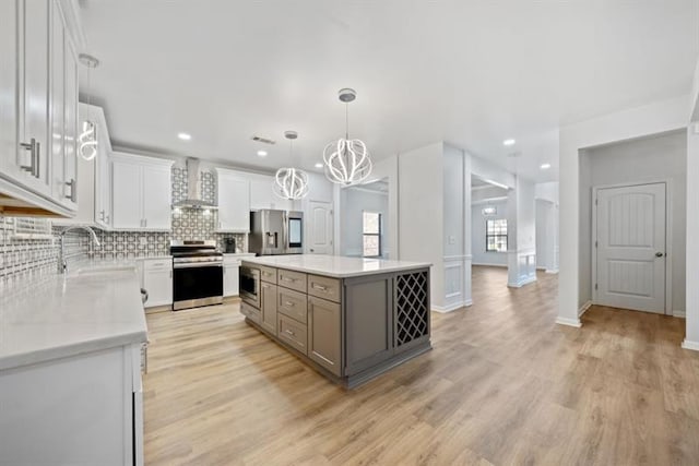 kitchen with appliances with stainless steel finishes, wall chimney exhaust hood, white cabinets, a center island, and sink