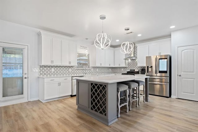 kitchen with white cabinetry, hanging light fixtures, a kitchen island, appliances with stainless steel finishes, and a kitchen bar