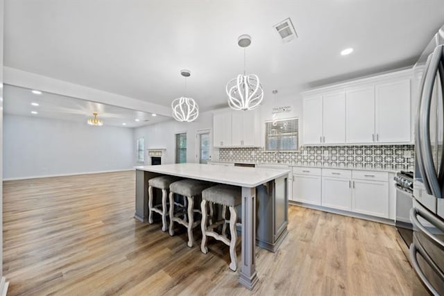 kitchen featuring tasteful backsplash, hanging light fixtures, stainless steel appliances, white cabinets, and a kitchen island