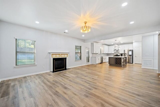 unfurnished living room featuring a notable chandelier and light wood-type flooring