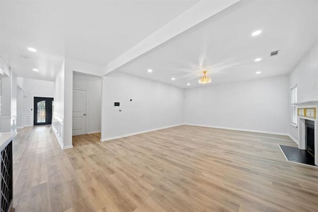 unfurnished living room with light wood-type flooring and an inviting chandelier