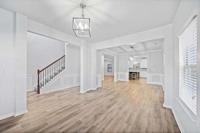 unfurnished living room with an inviting chandelier and light hardwood / wood-style flooring