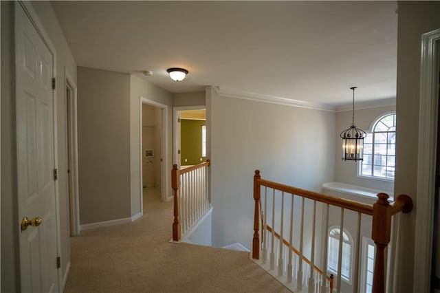 hallway with an inviting chandelier, carpet, ornamental molding, an upstairs landing, and baseboards