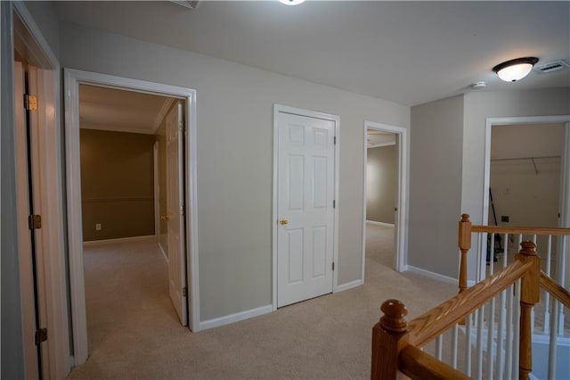 corridor with an upstairs landing, light colored carpet, baseboards, and visible vents
