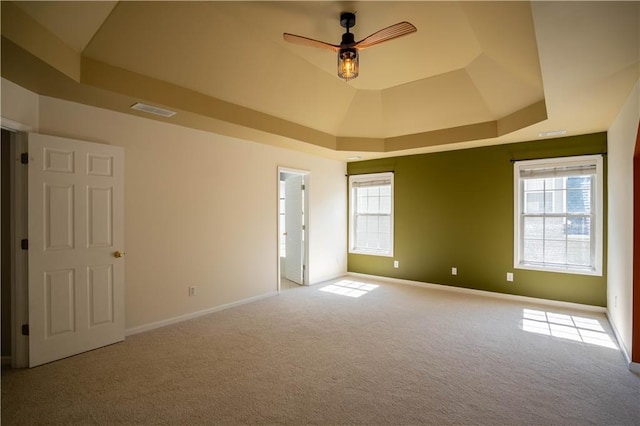 empty room featuring visible vents, plenty of natural light, a ceiling fan, carpet, and a tray ceiling