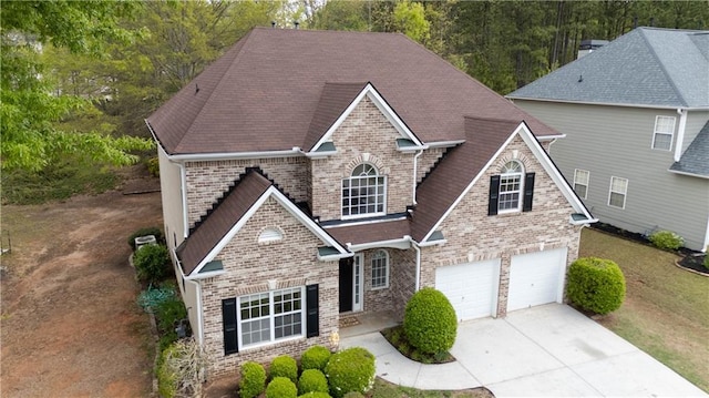 traditional-style house with a garage, brick siding, driveway, and a shingled roof