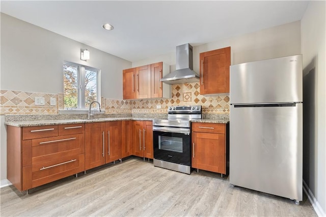 kitchen with light wood-type flooring, stainless steel appliances, tasteful backsplash, and wall chimney range hood