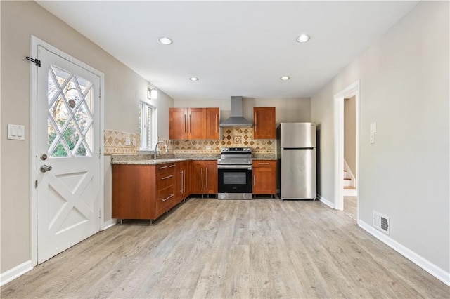 kitchen with decorative backsplash, light hardwood / wood-style floors, wall chimney range hood, and appliances with stainless steel finishes