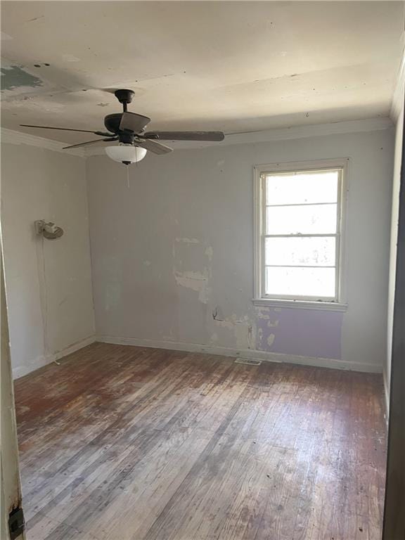 spare room with a ceiling fan, visible vents, baseboards, wood-type flooring, and crown molding