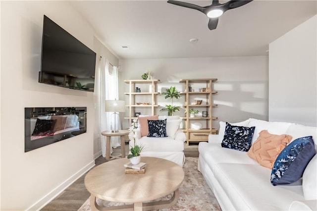living room featuring baseboards, ceiling fan, a glass covered fireplace, and wood finished floors