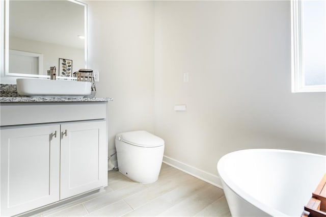 full bath with a freestanding bath, baseboards, vanity, and toilet