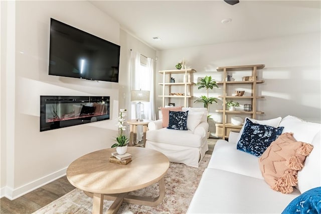 living area with baseboards, a glass covered fireplace, and wood finished floors