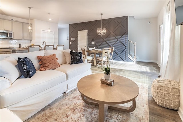 living room with light wood-style floors, baseboards, a notable chandelier, and stairway