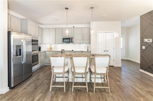 kitchen featuring backsplash, a center island with sink, wood finished floors, baseboards, and stainless steel appliances