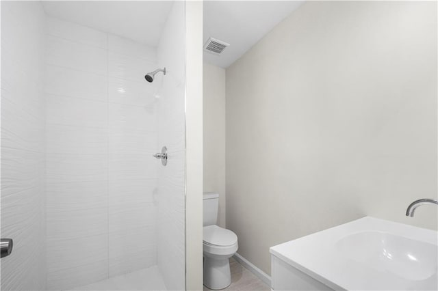 bathroom with a tile shower, vanity, and toilet