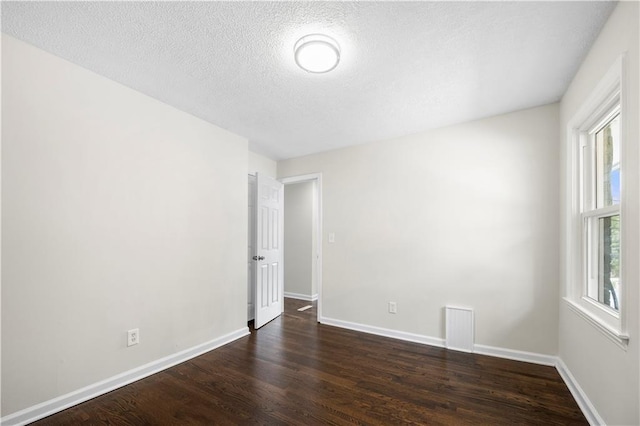 spare room featuring a textured ceiling, dark hardwood / wood-style floors, and plenty of natural light