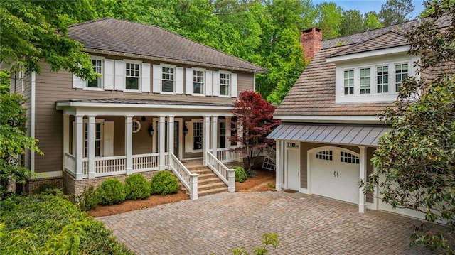view of front of house with a chimney, a porch, decorative driveway, and a garage