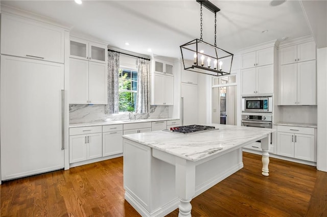 kitchen featuring stainless steel appliances, a kitchen island, backsplash, white cabinetry, and glass insert cabinets