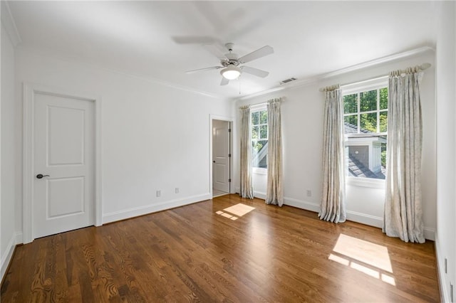 spare room featuring ceiling fan, wood finished floors, baseboards, and crown molding