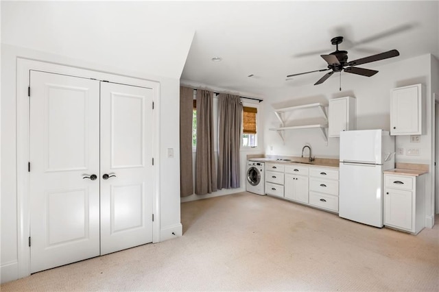 kitchen with freestanding refrigerator, washer / clothes dryer, light carpet, and white cabinets