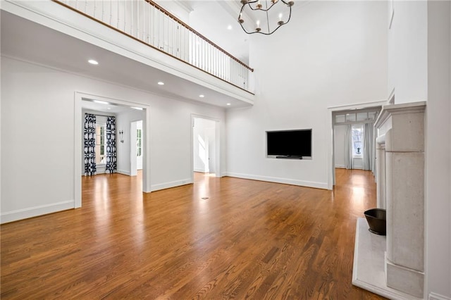 unfurnished living room featuring healthy amount of natural light, a high ceiling, wood finished floors, baseboards, and recessed lighting