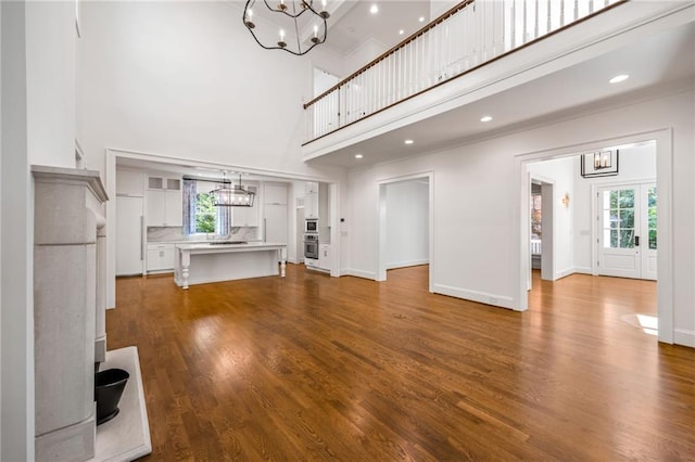 unfurnished living room featuring a chandelier, a towering ceiling, wood finished floors, and baseboards
