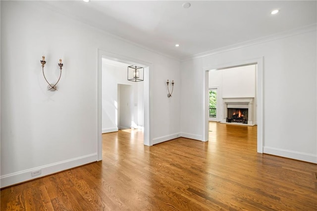 unfurnished living room with ornamental molding, wood finished floors, baseboards, recessed lighting, and a warm lit fireplace