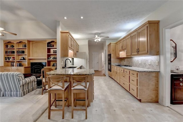 kitchen with a ceiling fan, a sink, light stone counters, freestanding refrigerator, and a peninsula