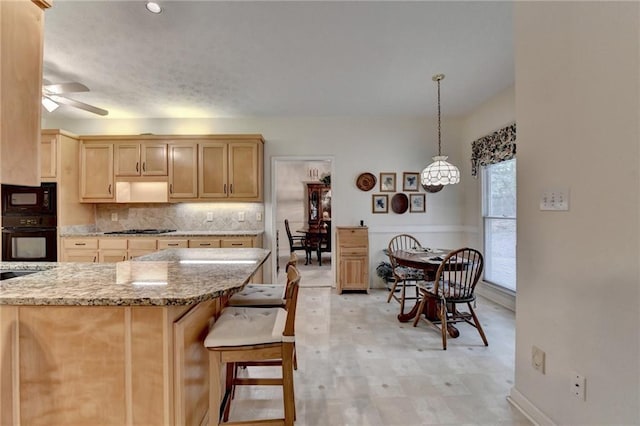 kitchen featuring black microwave, tasteful backsplash, light stone countertops, gas stovetop, and light floors