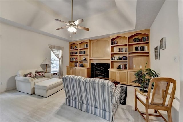living area with a raised ceiling, ceiling fan, light carpet, and a fireplace