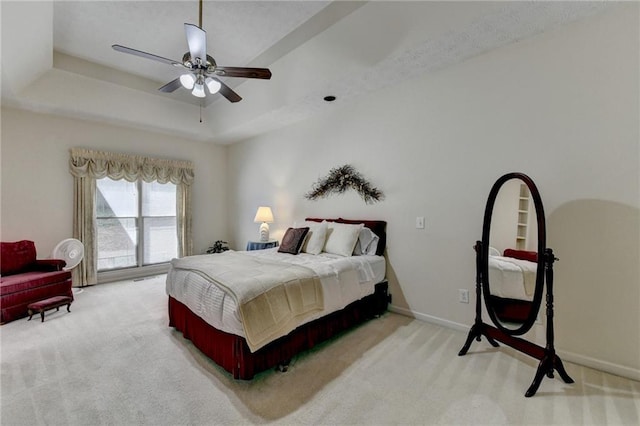 bedroom featuring a ceiling fan, a tray ceiling, light colored carpet, and baseboards
