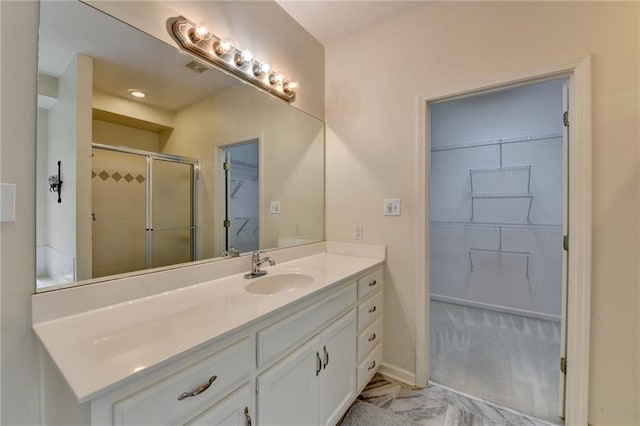 bathroom featuring vanity, baseboards, a walk in closet, and a shower stall