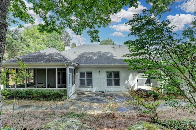 rear view of property with roof with shingles, stucco siding, a sunroom, a chimney, and a patio
