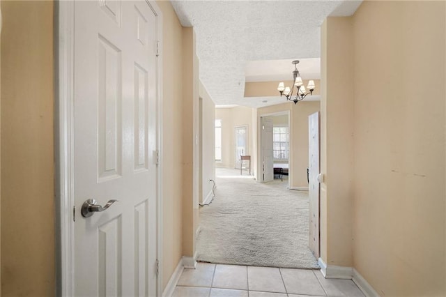 hall with light carpet, a notable chandelier, and a textured ceiling