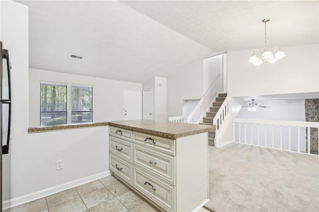 kitchen featuring lofted ceiling, cream cabinetry, hanging light fixtures, light carpet, and kitchen peninsula