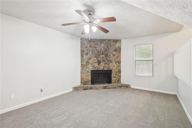 unfurnished living room with ceiling fan, a stone fireplace, and carpet