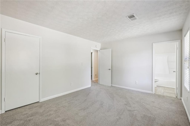 unfurnished bedroom featuring ensuite bathroom, a textured ceiling, multiple windows, and light colored carpet