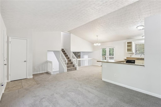 unfurnished living room featuring french doors, light carpet, a textured ceiling, and vaulted ceiling