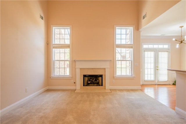 unfurnished living room featuring a fireplace with flush hearth, carpet flooring, baseboards, visible vents, and a notable chandelier