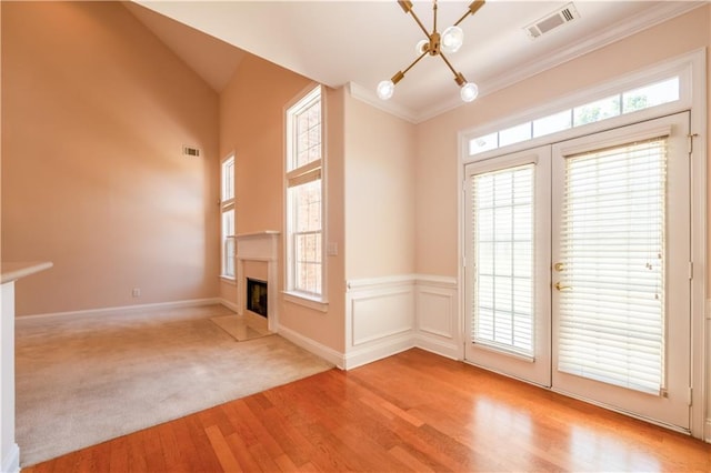 interior space with a fireplace with flush hearth, light wood-style flooring, visible vents, a notable chandelier, and crown molding