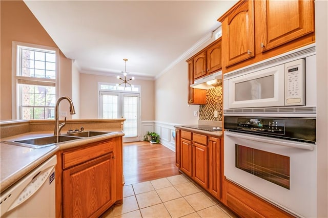 kitchen featuring a sink, brown cabinetry, ornamental molding, white appliances, and under cabinet range hood