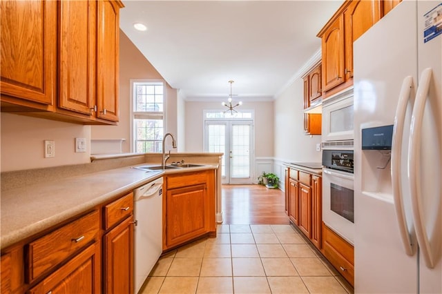 kitchen with an inviting chandelier, white appliances, a sink, and brown cabinets