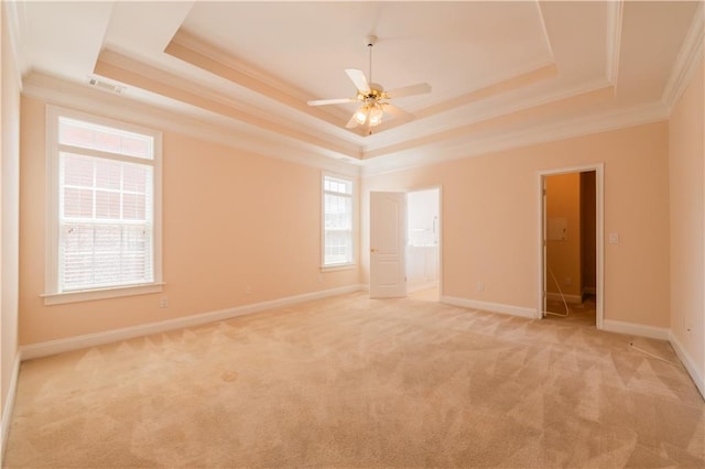 empty room with crown molding, a ceiling fan, a tray ceiling, light colored carpet, and baseboards