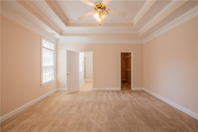 unfurnished bedroom featuring ornamental molding, light colored carpet, a walk in closet, and a raised ceiling