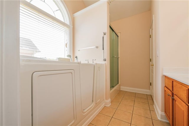 bathroom featuring a shower with shower door, tile patterned floors, vanity, baseboards, and washer / clothes dryer