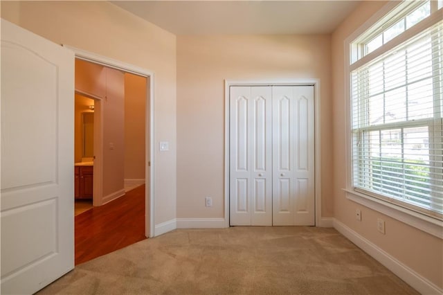 unfurnished bedroom with light carpet, baseboards, and a closet